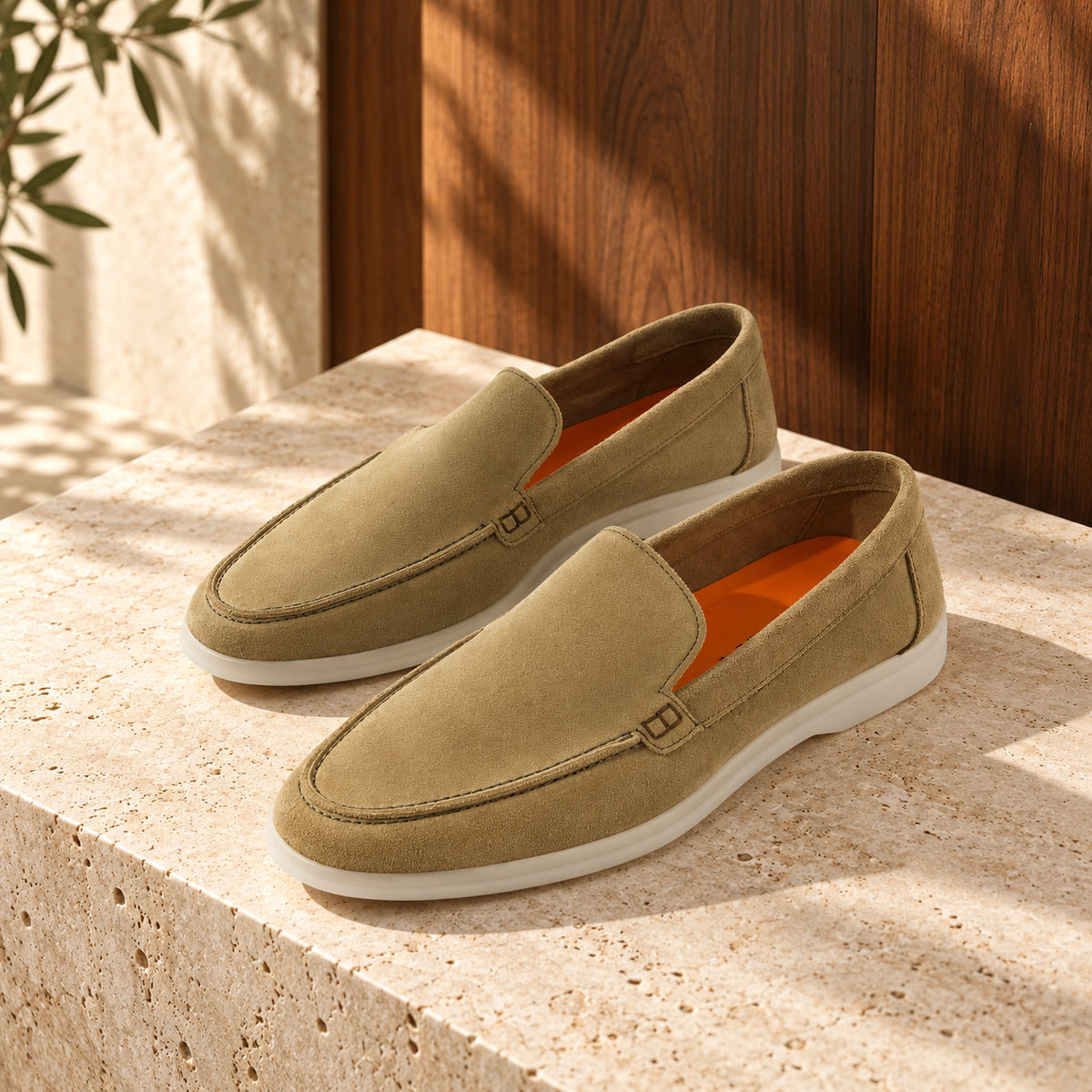 Loafers olive din piele întoarsă olive, cu talpă albă, așezați pe un soclu de travertin.