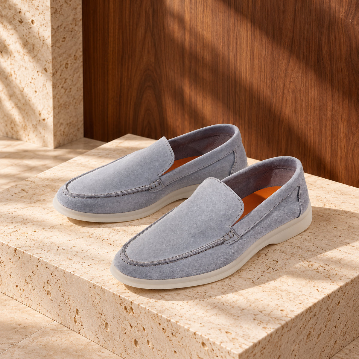 Loafers sky din piele întoarsă bleu-gri, cu talpă albă, așezați pe un soclu de travertin.