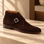 Ghete casual Dubai Suede din piele întoarsă, de culoare maro. Vedere din unghi pe o suprafață de piatră, în decor cu lemn.