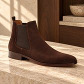 Ghete Chelsea Dark Brown Suede din piele întoarsă, de culoare maro închis. Vedere din unghi pe o suprafață de piatră, în decor cu lemn.