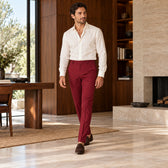 Pantaloni Santander burgundy, purtați pe model cu un top ivoire și mocasini maro, într-un interior cu lemn de nuc Cadru integral în mers.