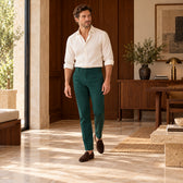 Pantaloni Sevilla verde închis, purtați pe model cu un top ivoire și mocasini maro, într-un interior cu lemn de nuc Cadru integral în mers.