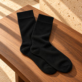 Pereche de șosete Black Tie negre, așezate natural pe o suprafață de piatră. Pereche așezată pe lemn, în lumină naturală.