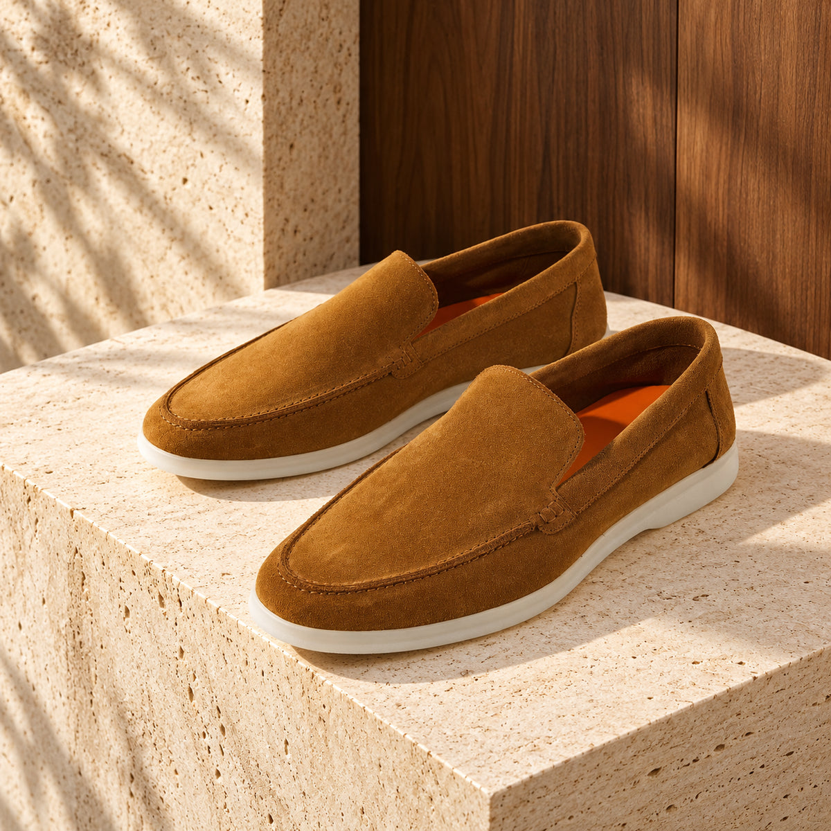 Loafers capri din piele întoarsă maro, cu talpă albă, așezați pe un soclu de travertin.