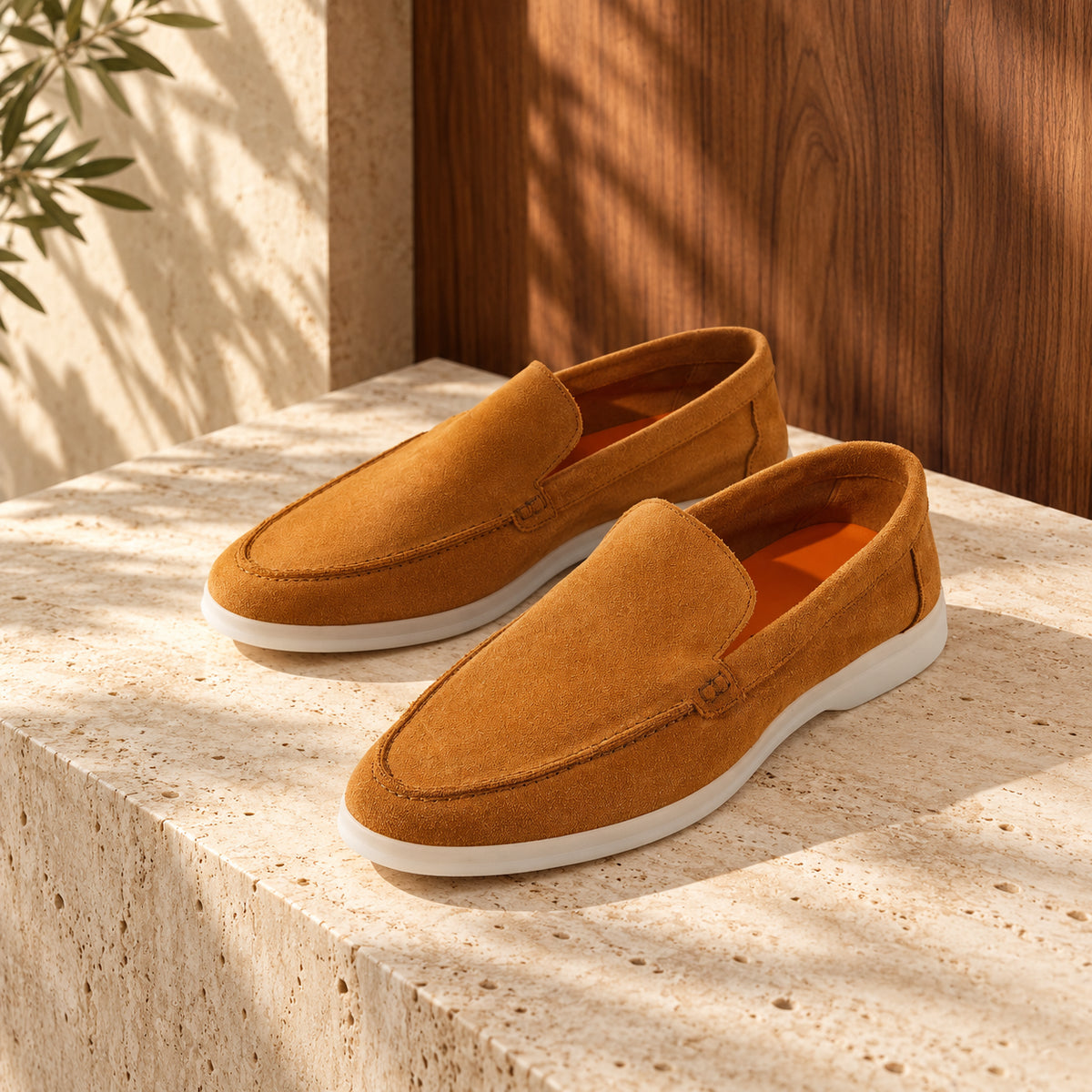 Loafers caramel din piele întoarsă caramel, cu talpă albă, așezați pe un soclu de travertin.