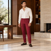 Pantaloni Santander burgundy, purtați pe model cu un top ivoire și mocasini maro, într-un interior cu lemn de nuc.