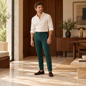 Pantaloni Sevilla verde închis, purtați pe model cu un top ivoire și mocasini maro, într-un interior cu lemn de nuc.